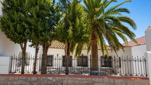 A building with a white facade, a tiled roof, and a wrought iron fence.