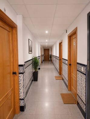 Pasillo de hotel con puertas de madera, baldosas estampadas y una planta en maceta.