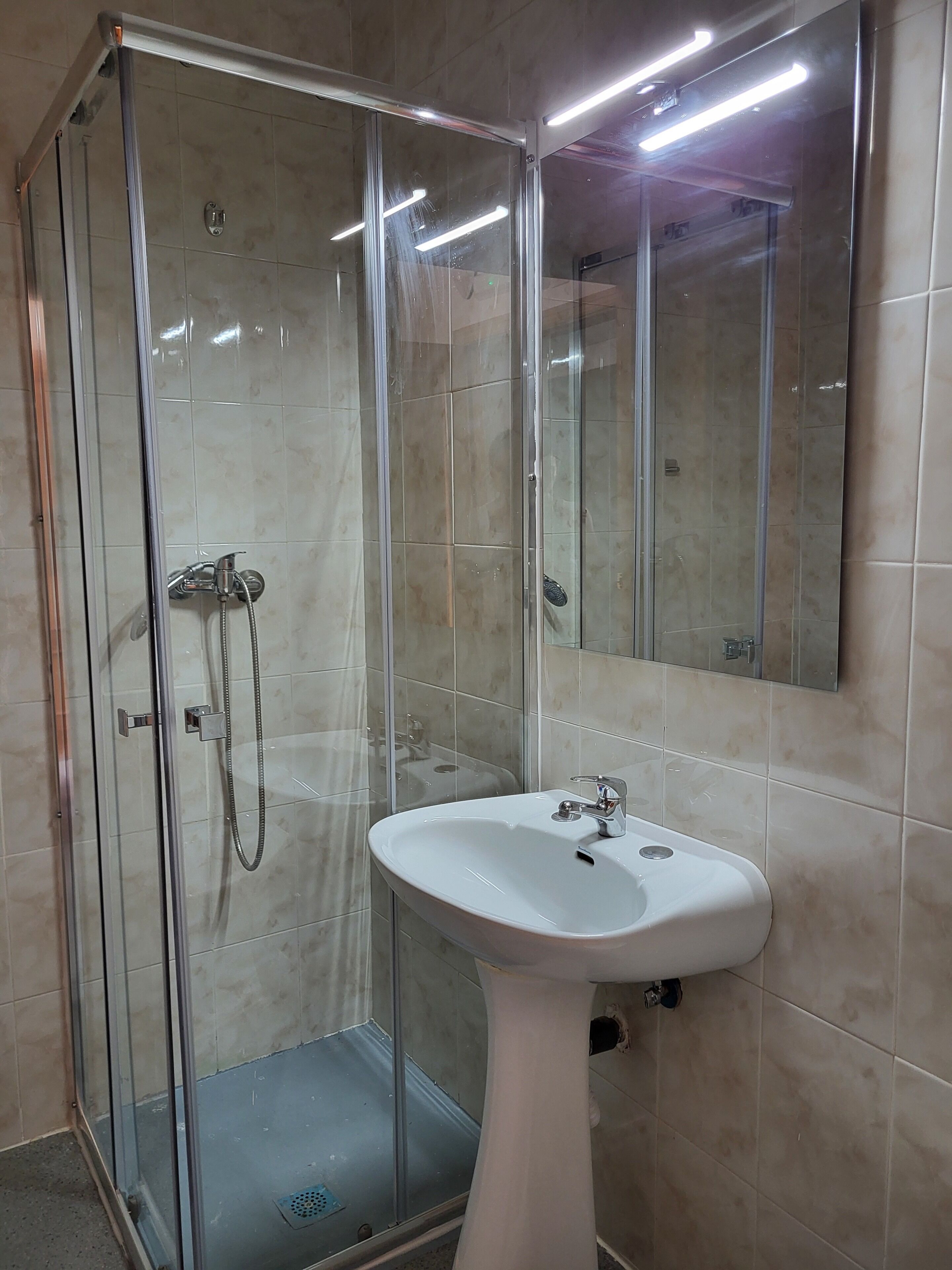 Un baño con ducha de vidrio, un lavamanos blanco y un espejo.