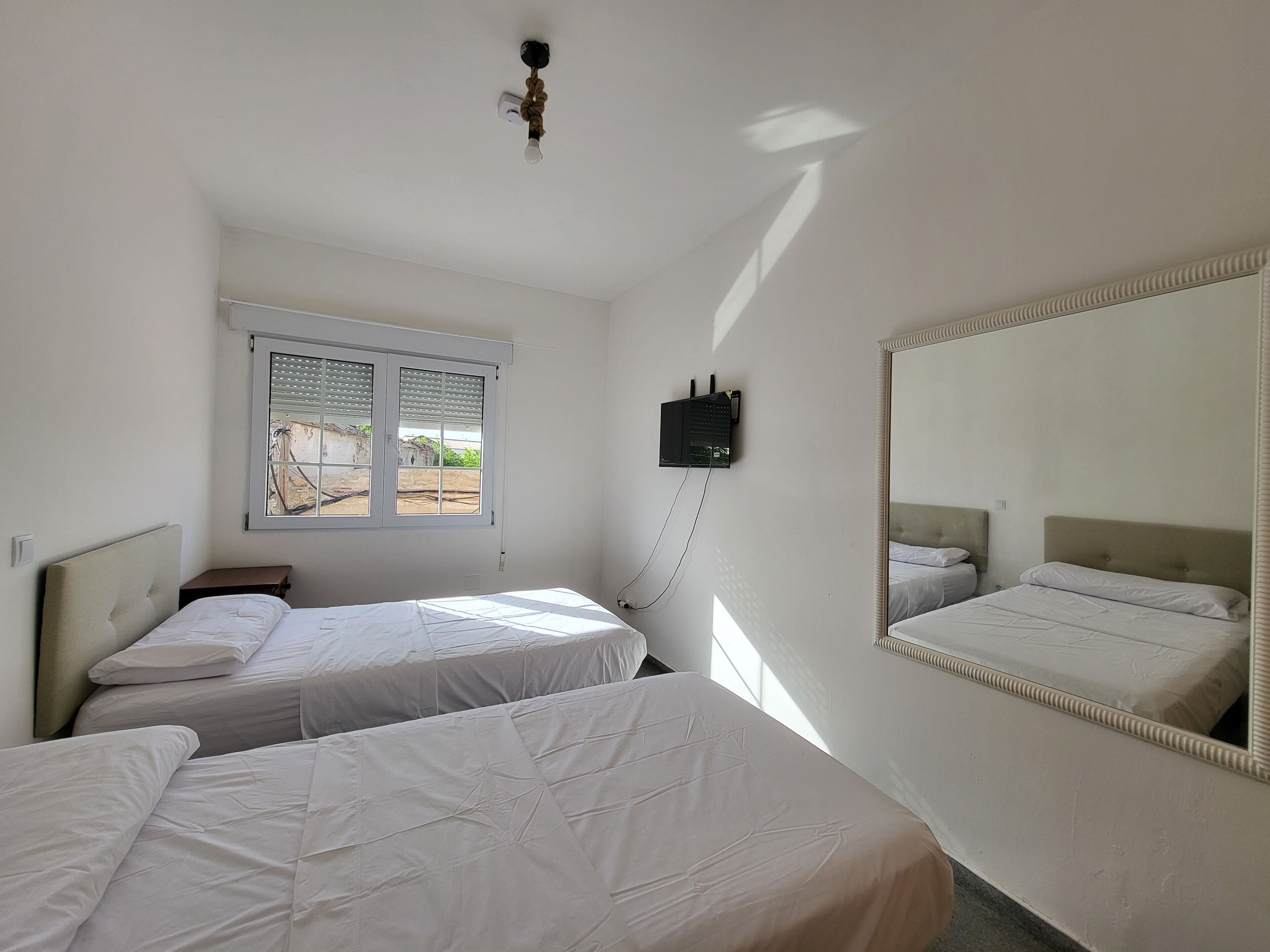 Habitación con dos camas, una ventana, televisor de pared y ventilador de techo.