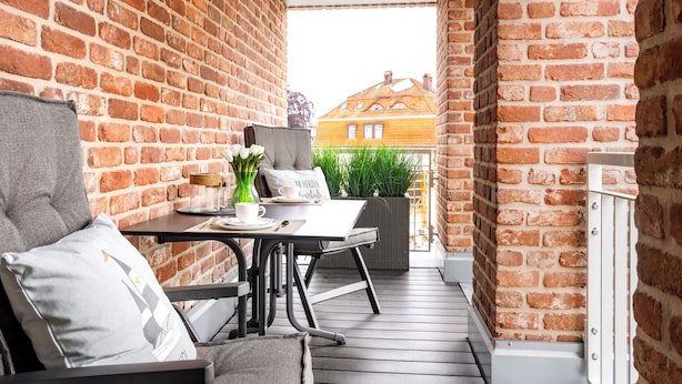 Ein Balkon mit Backsteinmauer, einem Tisch mit Blumenvasen und einem Stuhl.