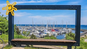 Ein Yachthafen mit zahlreichen vertäuten Booten, einem strahlend blauen Himmel und einer hölzernen Bank im Vordergrund.