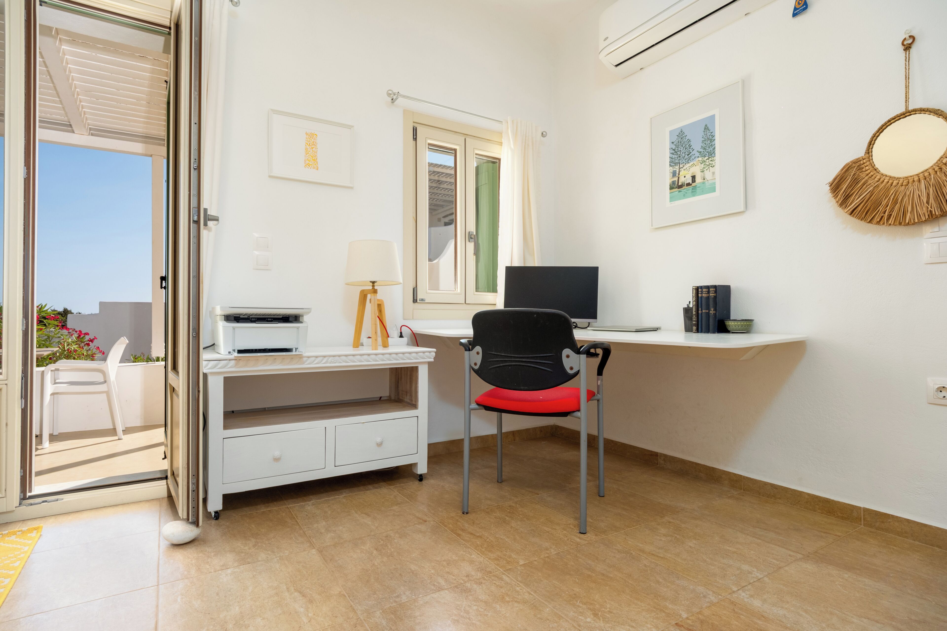 Una habitación con escritorio, silla, impresora, lámpara y ventana con vistas.