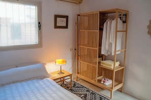 Ein Schlafzimmer mit einem Bett, einer Nachttischlampe, einem Kleiderschrank und einem Fenster.