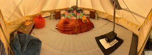 Une tente avec un tapis à motifs, un lit avec une literie colorée, une petite boîte en bois et une lampe suspendue.