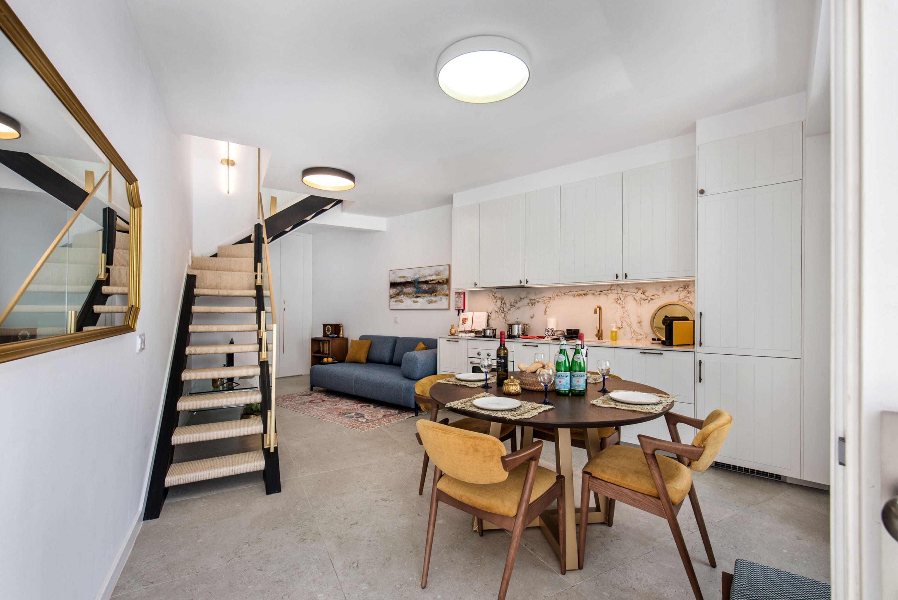 A modern interior with a staircase, dining area, sofa, and kitchen.