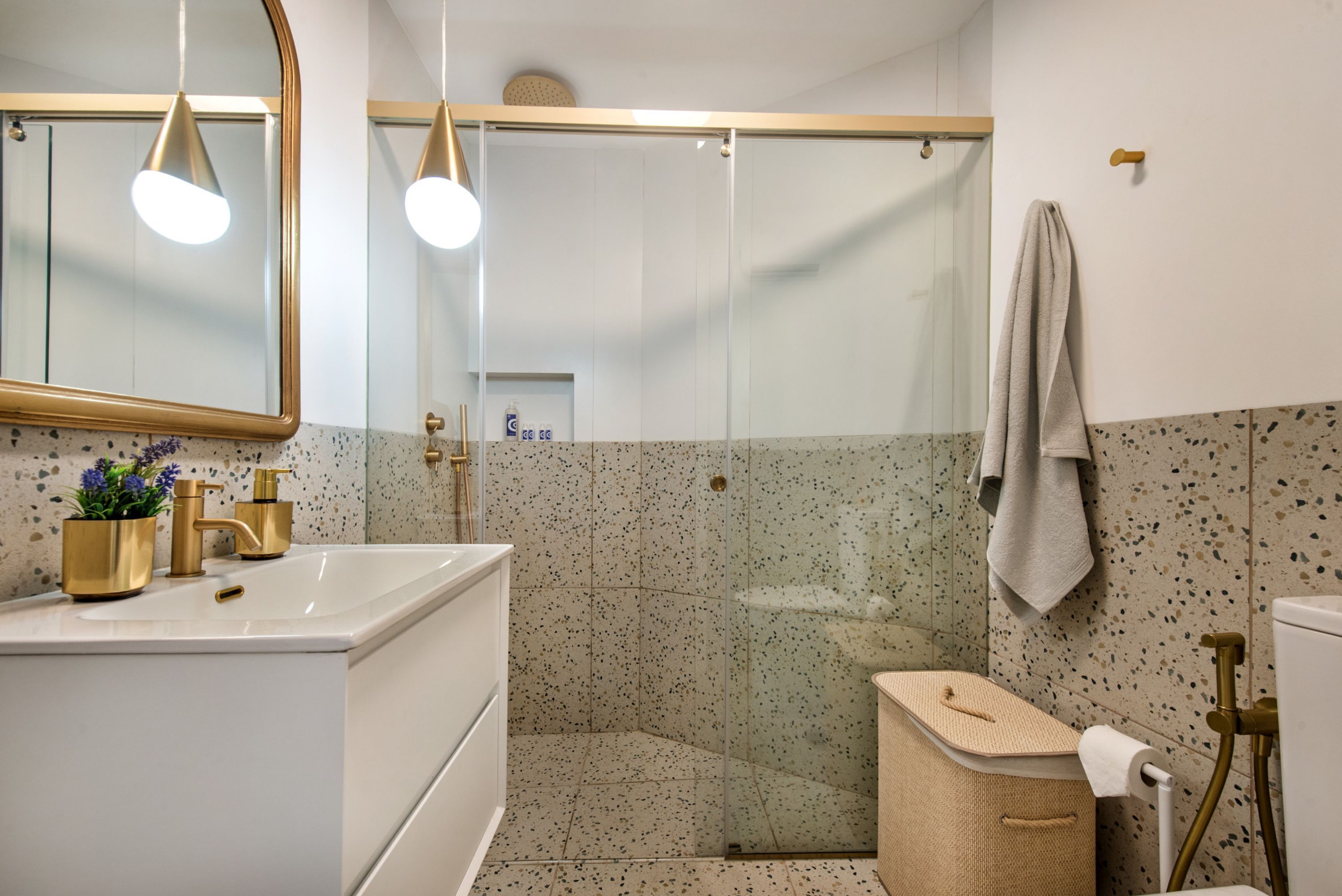 A modern bathroom with a white sink, gold fixtures, a glass shower enclosure, and a towel hanging on the wall.