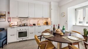 A modern kitchen with white cabinets, a dining table set for four, and a clock on the wall. - Casa Portuguesa in Tavira (Tavira)