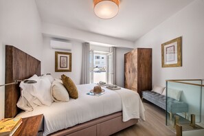 Ein modernes Schlafzimmer mit einem großen Bett, einem Nachttisch, einer Leselampe, einem Fenster mit Vorhängen und Blick auf Gebäude.