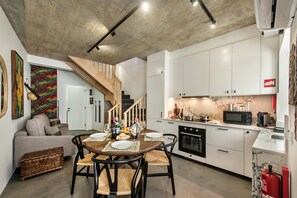 Eine moderne Küche mit weißen Schränken, ein Essbereich mit Holztisch und eine Treppe, die zu einer weiteren Ebene führt.