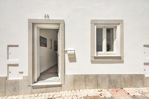 Ein weißes Gebäude mit einer Tür, die zu einem Innenflur führt, einem Fenster und einem Briefkasten.