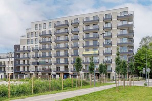 A multi-story residential building with balconies, a paved sidewalk, and greenery. - Stylish Apartment with Garden | Quiet Neighborhood (Warszawa)