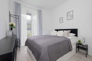 Ein Schlafzimmer mit Bett, Schreibtisch, Stuhl, Nachttisch und einem Fenster mit Vorhängen.