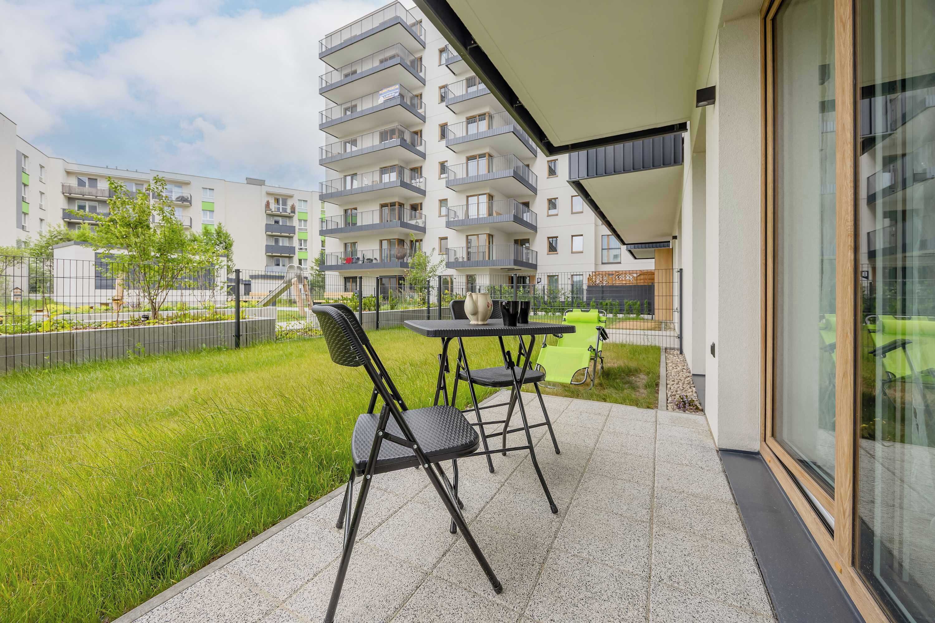 Ein Balkon mit Tisch und Stühlen, eine Rasenfläche und ein mehrstöckiges Gebäude im Hintergrund.