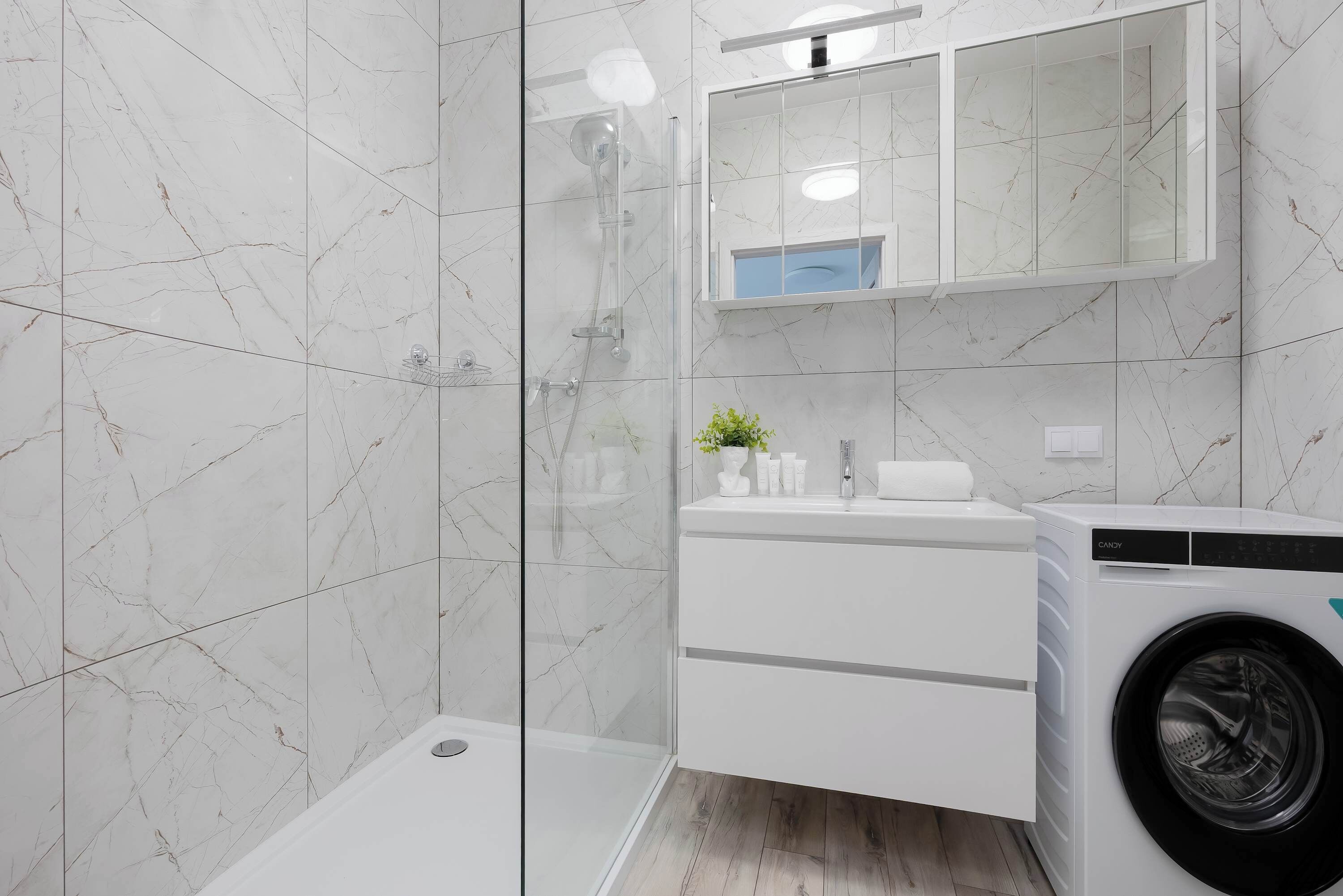 Un baño moderno con cabina de ducha de vidrio, lavabo empotrado con espejo y lavadora de carga frontal.