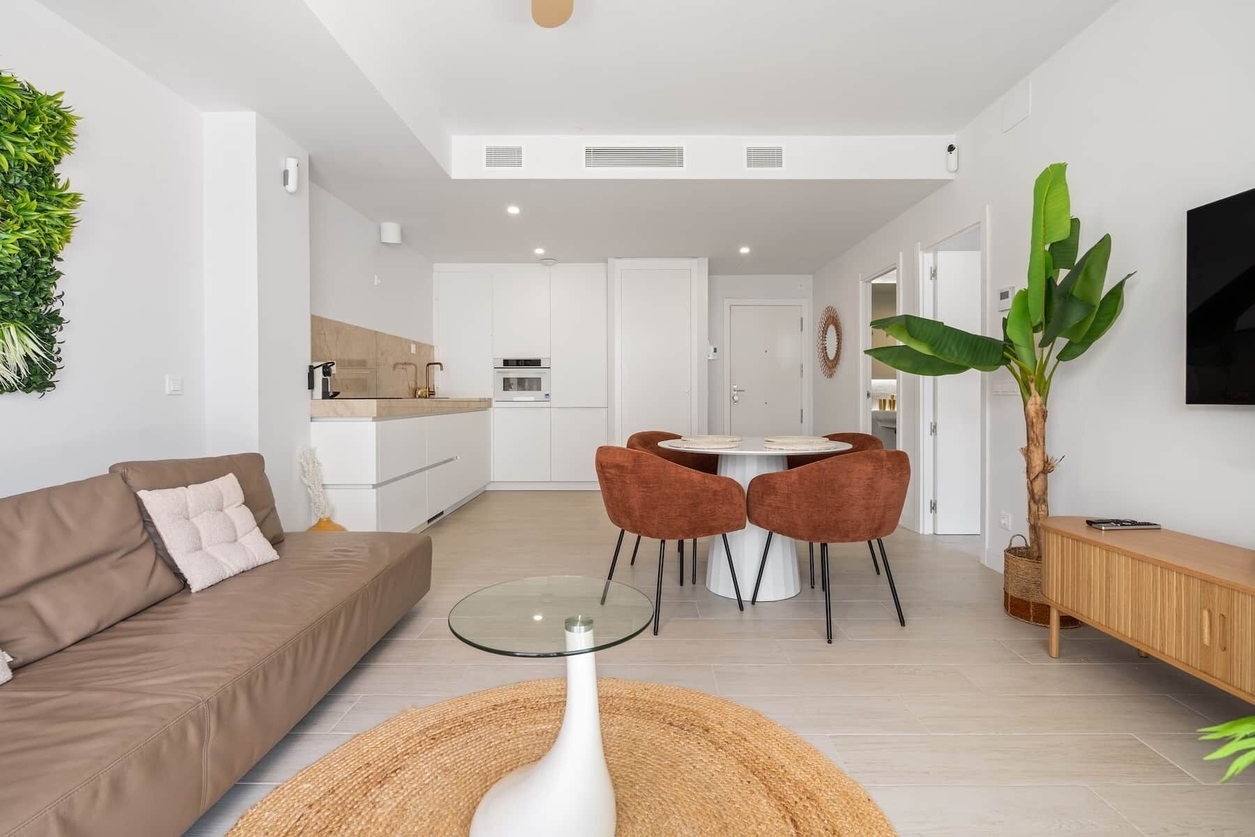 Una sala de estar moderna con un sofá, una mesa de centro de vidrio y una zona de comedor con sillas.