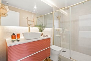 Ein modernes Badezimmer mit einem weißen Waschbecken, einer Duschkabine aus Glas und einer roten Kommode.