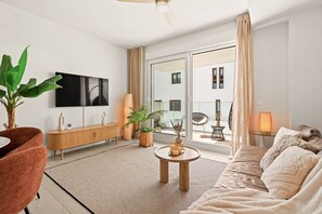 Ein modernes Wohnzimmer mit Sofa, Couchtisch, Fernseher und einem Balkon mit Gartenmöbeln.