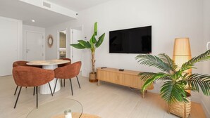 Un salon moderne comprenant un coin repas, un téléviseur fixé au mur et une grande plante en pot.