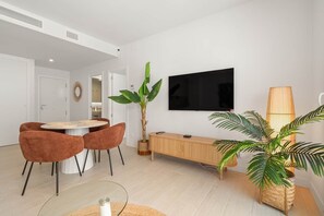 Ein modernes Wohnzimmer mit Essbereich, einem an der Wand montierten Fernseher und einer großen Topfpflanze.