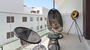 Un balcon avec deux fauteuils en osier, un fauteuil suspendu et un lampadaire.