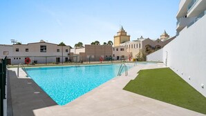 Une piscine à l’eau d’un bleu cristallin, entourée d’un bâtiment blanc doté d’un toit plat et d’une petite tour.