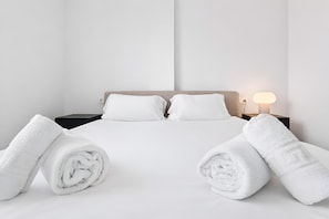 Ein Hotelzimmer mit einem Bett, zwei Kissen, einem Nachttisch, einer Lampe und zwei gerollten Handtüchern.