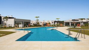 A swimming pool with steps, surrounded by modern buildings and palm trees. - RDR559 - Seaview 2 Bed Apartment in Habitat Valle Romano (Estepona)