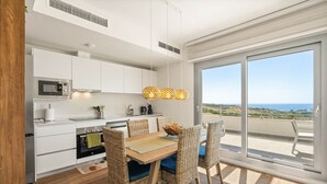 A modern kitchen with white cabinetry, a microwave, stove, and a dining area with wicker chairs and a wooden table. - RDR559 - Seaview 2 Bed Apartment in Habitat Valle Romano (Estepona)