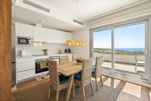 A modern kitchen with white cabinetry, a microwave, stove, and a dining area with wicker chairs and a wooden table. - RDR559 - Seaview 2 Bed Apartment in Habitat Valle Romano (Estepona)