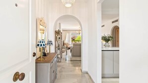 A hallway with a marble floor, white walls, and a chandelier. There is a kitchen area with a white countertop and a vase of flowers. - RDR548 - Stylish 2 bed apt in La Ola (Marbella)
