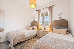 A hotel room with two beds, a window with curtains, a bedside table with lamps, and a wall-mounted light fixture. - RDR548 - Stylish 2 bed apt in La Ola (Marbella)