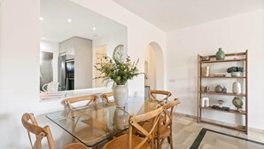 A dining area with a glass table, wooden chairs, a vase with flowers, and a bookshelf. - RDR548 - Stylish 2 bed apt in La Ola (Marbella)