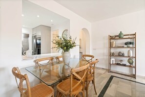 A dining area with a glass table, wooden chairs, a vase with flowers, and a bookshelf. - RDR548 - Stylish 2 bed apt in La Ola (Marbella)