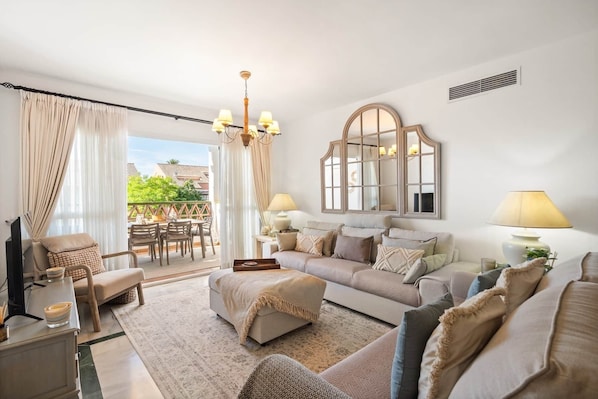 A living room with a sofa, ottoman, and a dining area with chairs and a table. - RDR548 - Stylish 2 bed apt in La Ola (Marbella)