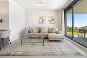 Ein modernes Wohnzimmer mit einer Couch, einem Glastisch und Blick ins Freie.