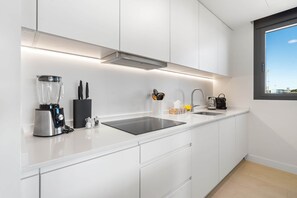 Eine moderne Küche mit weißen Schränken, einer Edelstahl-Spüle, einer eingebauten Dunstabzugshaube und einem Fenster mit Blick.