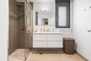 A modern bathroom with a glass shower enclosure, a white vanity with a mirror, and a wicker trash bin. - RDR556 - Modern 3-Bedroom Apartment in Camarate Hills (Casares)