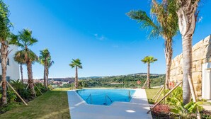 Ein Pool mit freiem Blick auf die umliegende Landschaft, Palmen und eine Steinmauer.