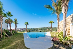 Ein Pool mit freiem Blick auf die umliegende Landschaft, Palmen und eine Steinmauer.