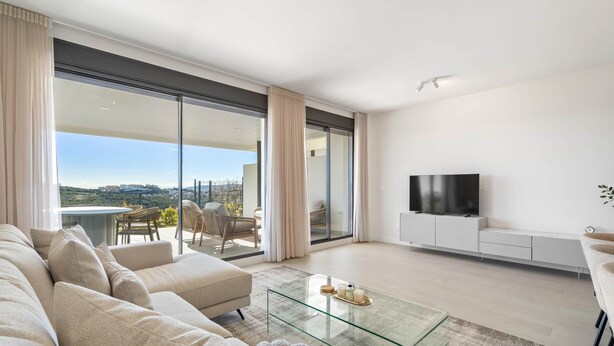 Ein modernes Wohnzimmer mit einer Couch, einem Glastisch, einem Flachbildfernseher und einem Balkon mit Blick.