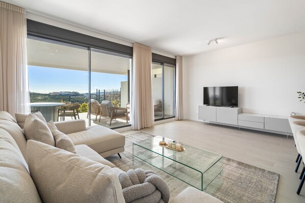 Ein modernes Wohnzimmer mit einer Couch, einem Glastisch, einem Flachbildfernseher und einem Balkon mit Blick.