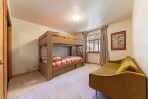Una camera da letto con un letto a castello, un divano, una finestra con tende e un quadro appeso al muro.