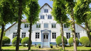 A large white building with a central entrance, surrounded by trees and well-maintained lawns.