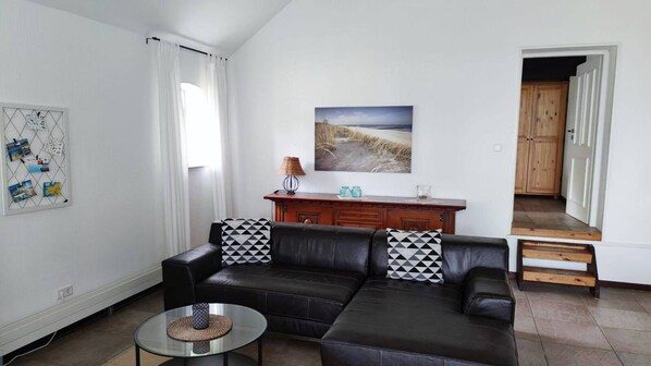 A living room with a black leather sofa, a small round table, a wooden cabinet, and a painting on the wall.
