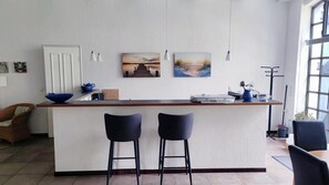 A kitchen with a central island, two bar stools, a white door, and two paintings on the wall.