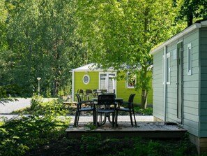 Een groene caravan met een terras, buitenmeubels en een fiets.