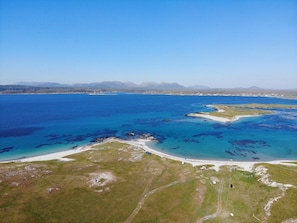 An aerial view of a coastal area with a beach, clear blue waters, and distant mountains.