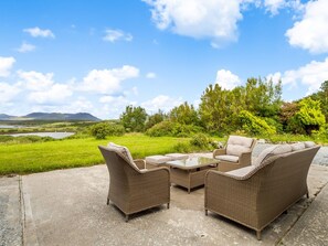 Korbmöbel im Freien auf einer Betonpatio mit Blick auf einen See und Hügel.