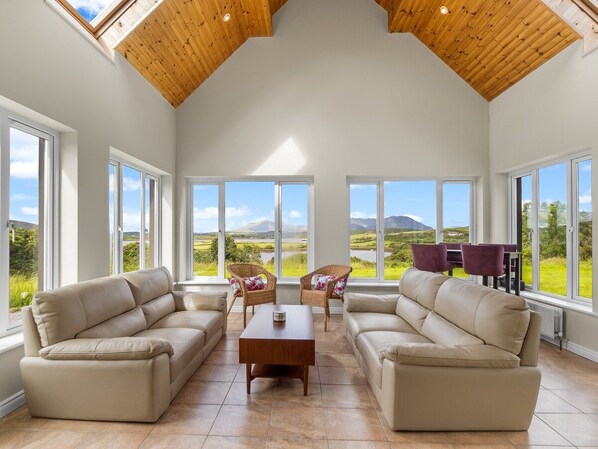 A spacious living room with high ceilings, large windows, and a view of the countryside.